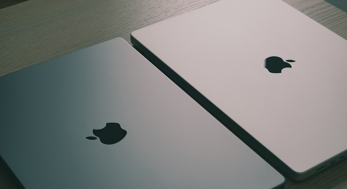 Two laptops sitting side by side on a wooden table for comparison.